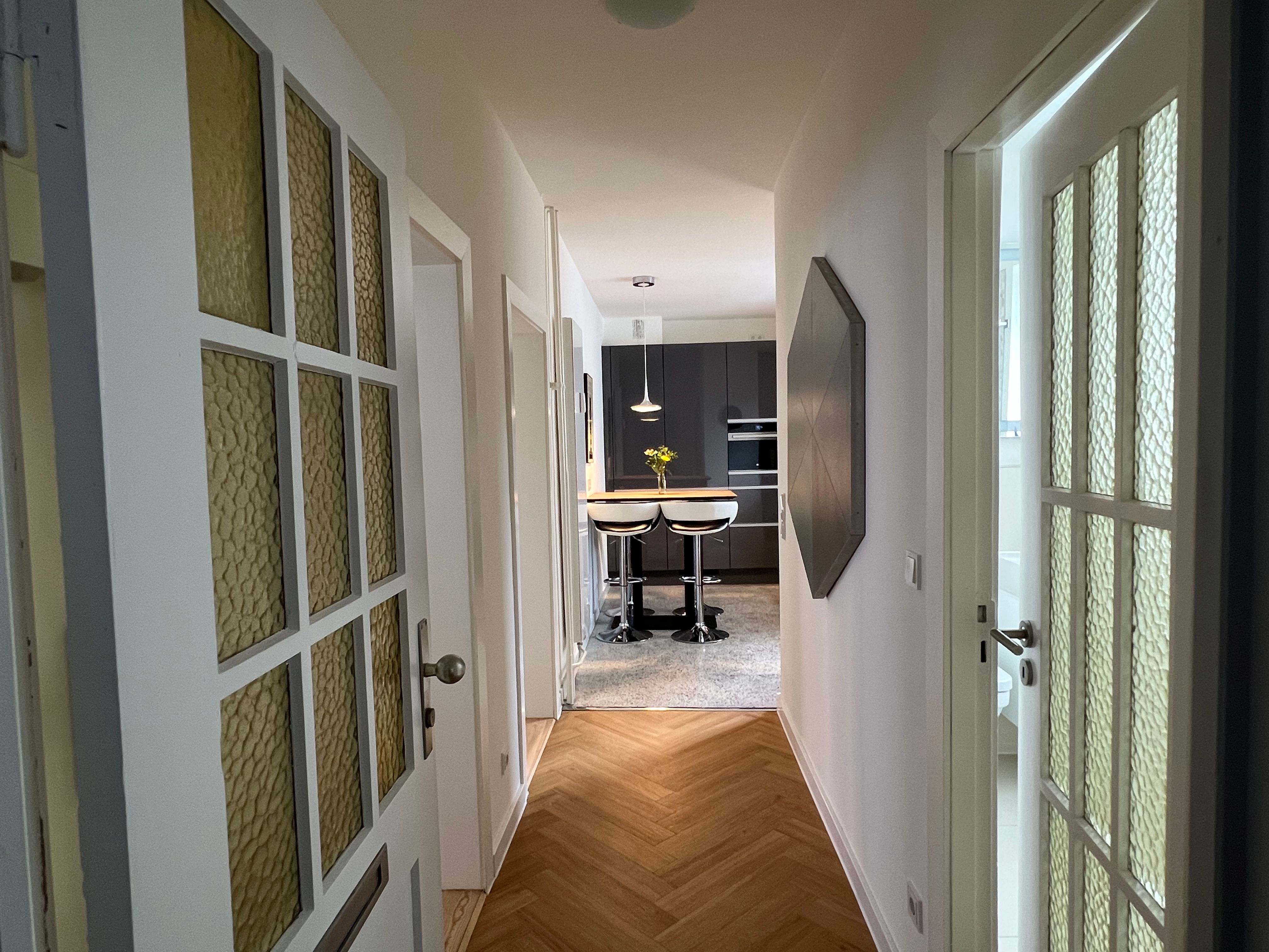 Heller Flur mit Dielenboden und Glastüren, Blick in Richtung Küche.