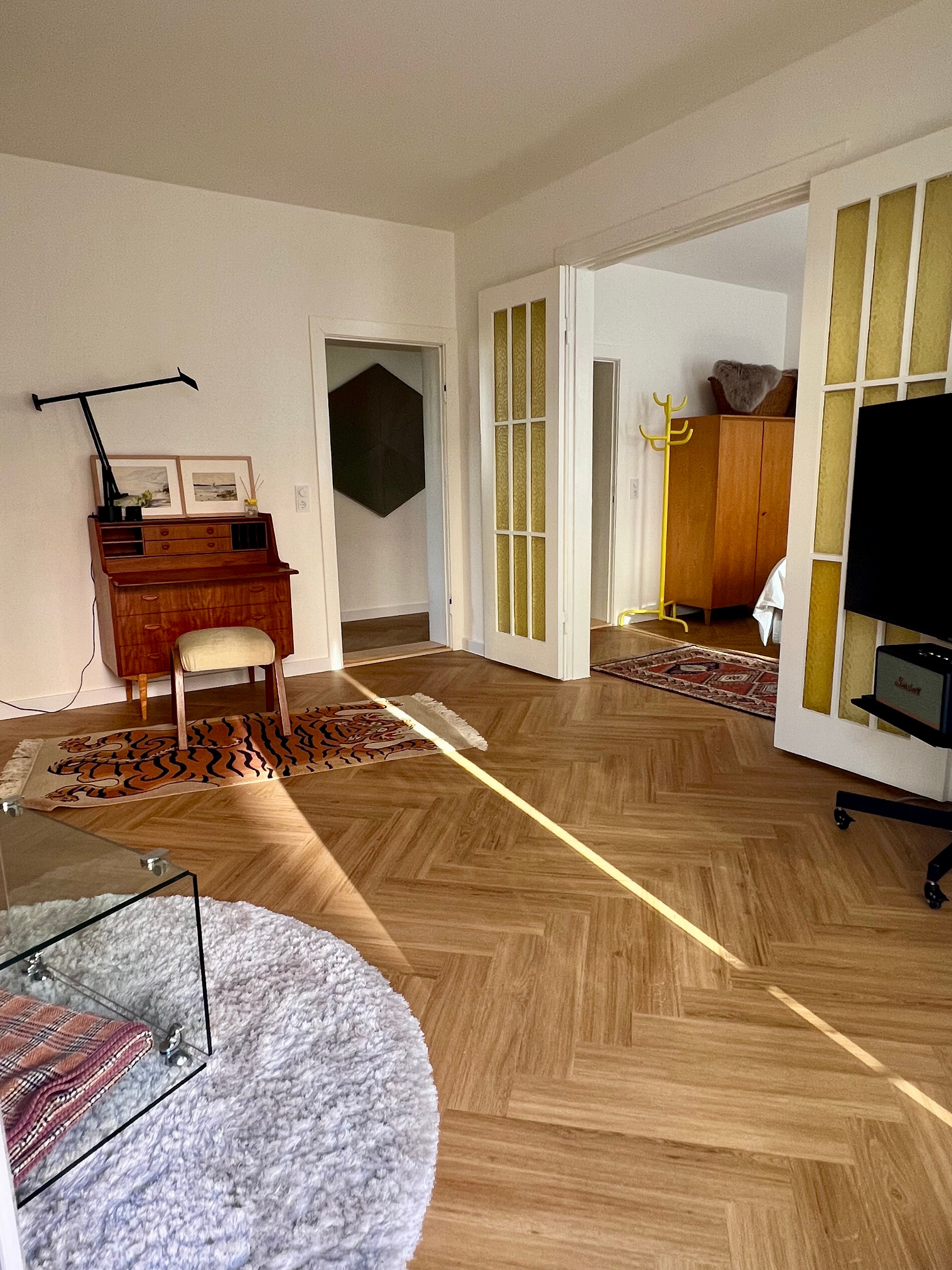Wohnzimmer mit Dreisitzer, Sessel, Couchtisch und Teppich auf hellem Dielenboden.