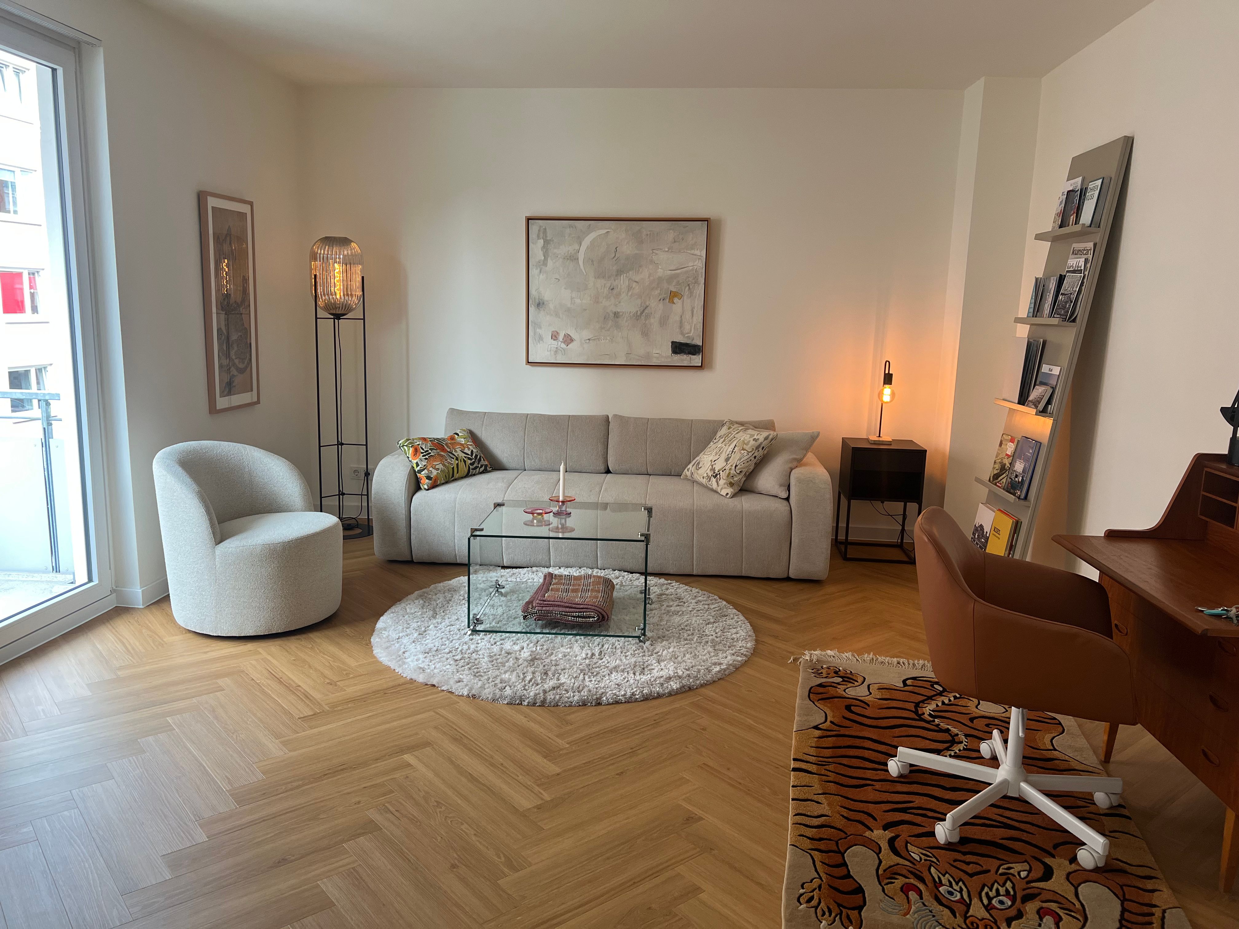Living room with open French doors, high ceilings and daylight; sofa, armchair and rug on pale plank flooring.